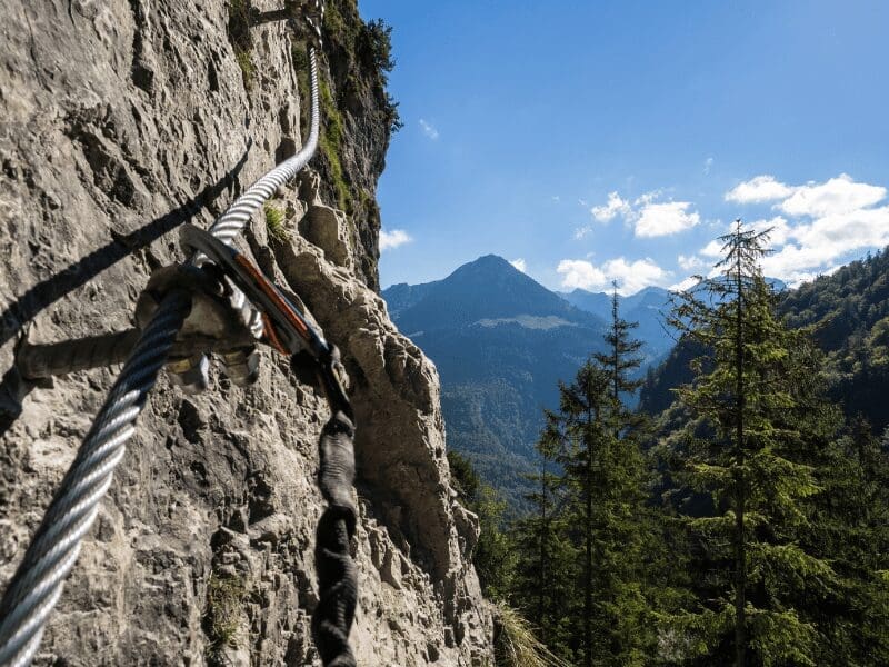 Câble de sécurité fixé sur une paroi rocheuse avec un paysage de montagne en arrière-plan, utilisé pour la via ferrata.